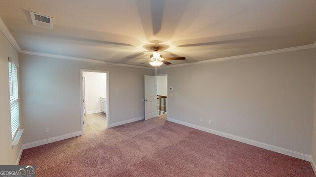 carpeted spare room featuring ornamental molding, visible vents, ceiling fan, and baseboards