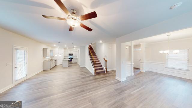 unfurnished living room featuring stairs, light wood-style floors, ceiling fan with notable chandelier, and wainscoting