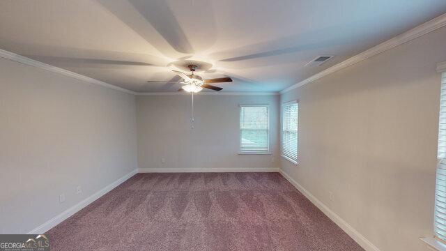 carpeted spare room with ceiling fan, baseboards, ornamental molding, and visible vents