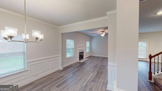 unfurnished living room with crown molding, wood finished floors, ceiling fan with notable chandelier, and stairs