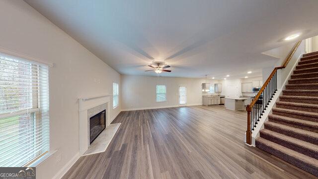unfurnished living room featuring a premium fireplace, wood finished floors, a ceiling fan, and stairway