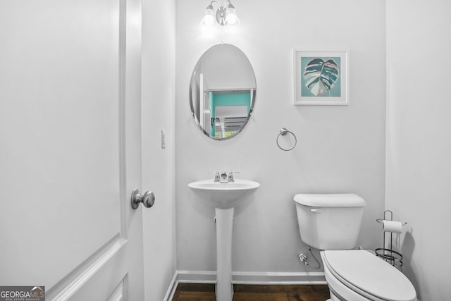 half bath with baseboards, toilet, and wood finished floors