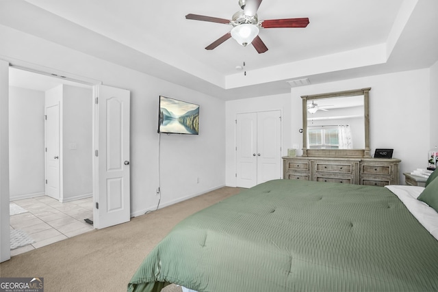 carpeted bedroom featuring a closet, baseboards, visible vents, a ceiling fan, and a tray ceiling