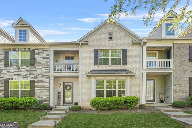 multi unit property with a front yard, a balcony, and brick siding