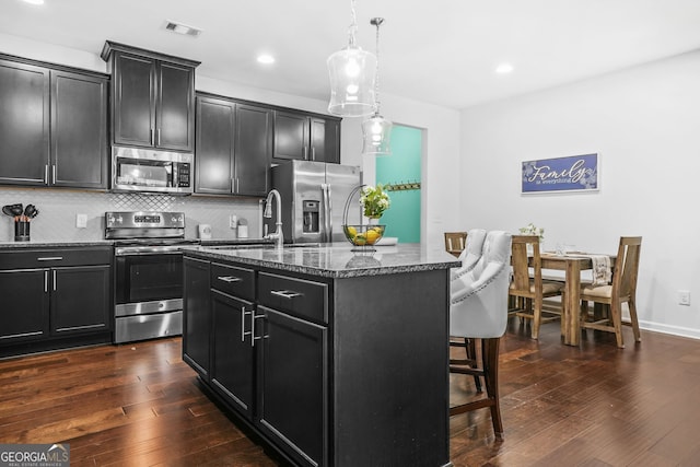 kitchen with dark cabinets, a breakfast bar, an island with sink, visible vents, and stainless steel appliances