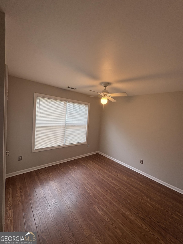 empty room featuring dark wood-type flooring, visible vents, baseboards, and a ceiling fan