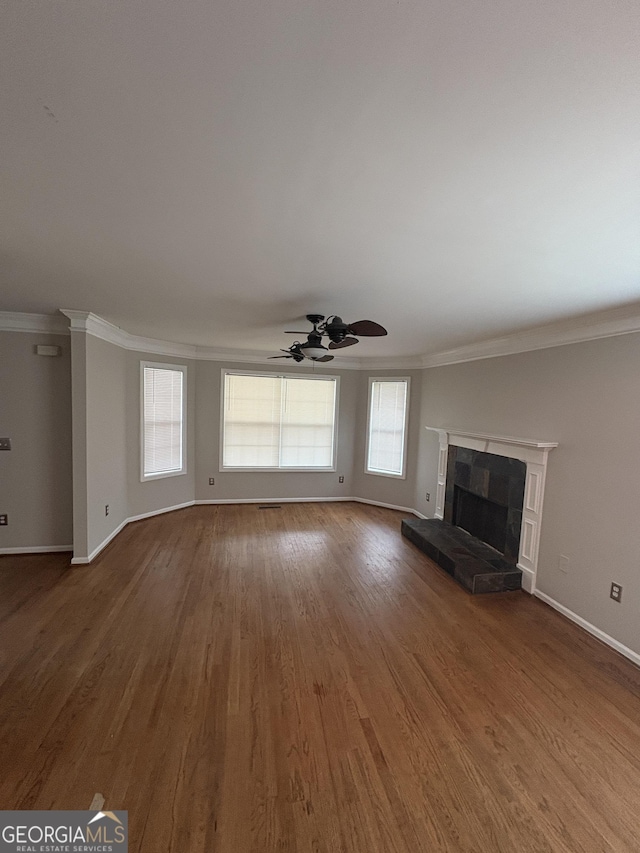 unfurnished living room with wood finished floors, baseboards, ornamental molding, and a wealth of natural light