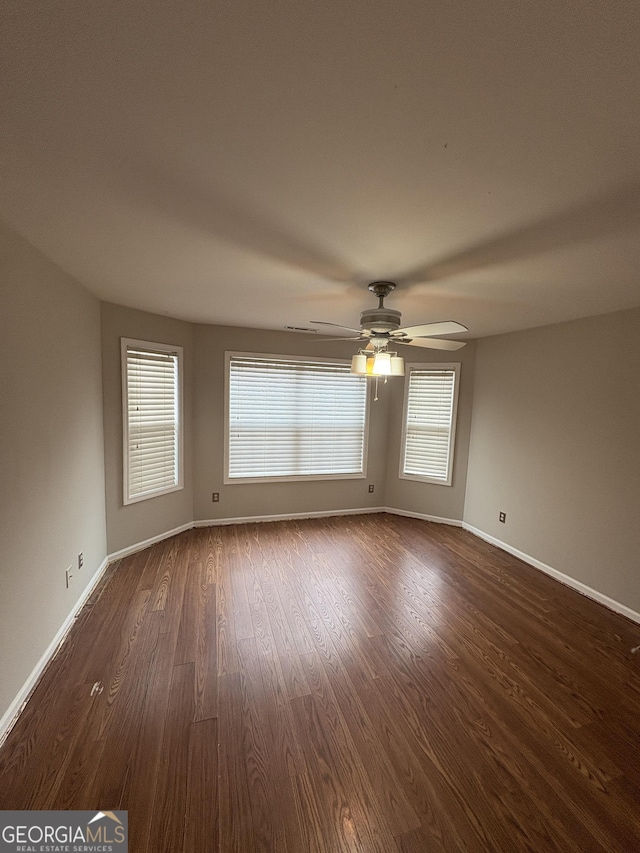 unfurnished room featuring dark wood-style flooring, ceiling fan, and baseboards