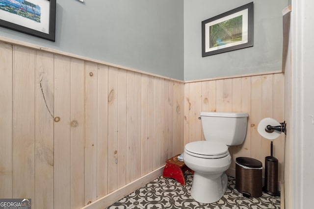 bathroom featuring toilet, wooden walls, and a wainscoted wall