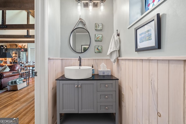 bathroom with wood finished floors, wooden walls, vanity, and a wainscoted wall