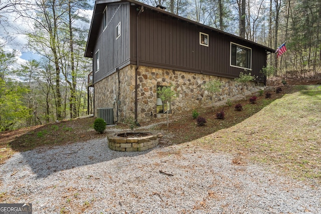 view of home's exterior with central AC, stone siding, and an outdoor fire pit