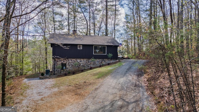 exterior space with dirt driveway and a view of trees