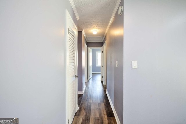 corridor featuring baseboards, ornamental molding, dark wood-style floors, a textured ceiling, and attic access