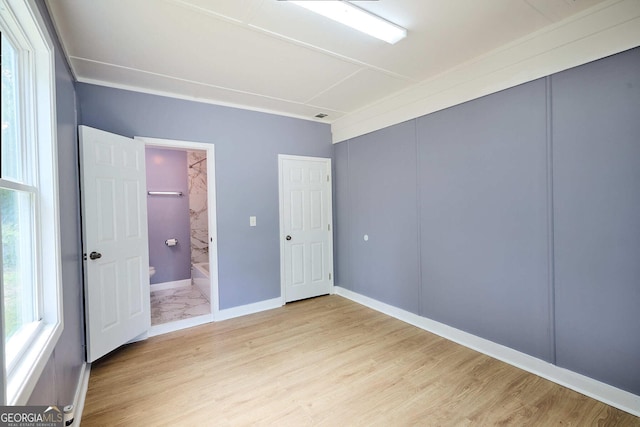 unfurnished bedroom featuring a closet, baseboards, light wood finished floors, and connected bathroom