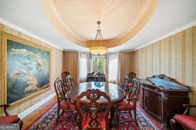 dining room with a raised ceiling, wallpapered walls, ornamental molding, and wood finished floors