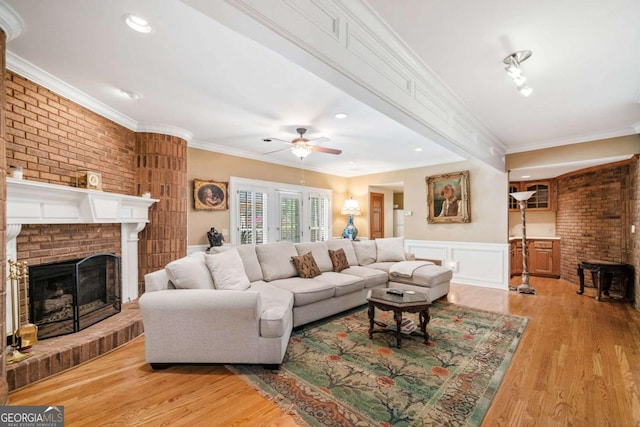 living area with ornamental molding, a ceiling fan, a brick fireplace, and light wood finished floors