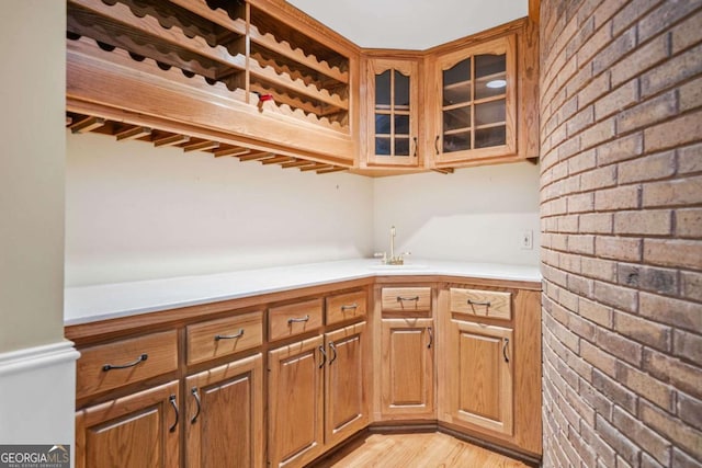 bar with brick wall, light wood-style floors, a sink, and wet bar