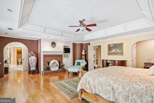 bedroom with arched walkways, wood finished floors, a brick fireplace, and visible vents