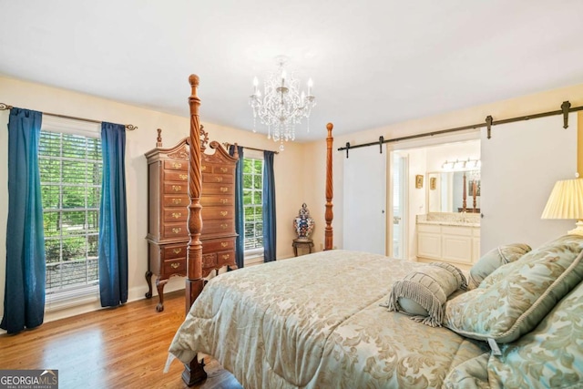 bedroom featuring baseboards, an inviting chandelier, a barn door, connected bathroom, and wood finished floors