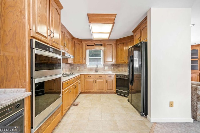 kitchen featuring black appliances, under cabinet range hood, light stone counters, a sink, and backsplash
