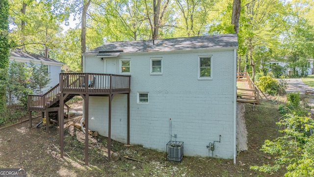 back of house with a shingled roof, brick siding, a deck, and stairs