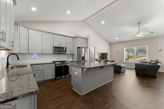 kitchen with stone counters, appliances with stainless steel finishes, a sink, open floor plan, and backsplash
