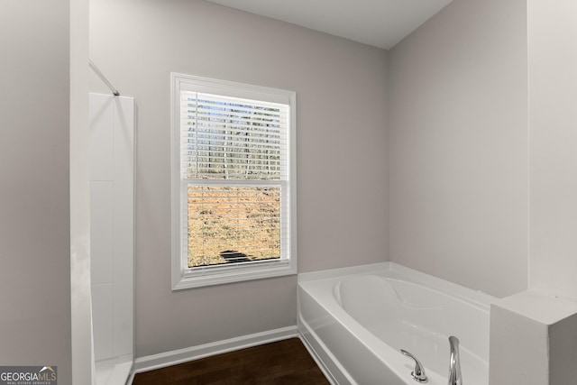 full bath featuring baseboards, a garden tub, and wood finished floors