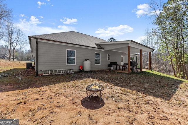 rear view of house with an outdoor fire pit, roof with shingles, a patio, and central AC unit