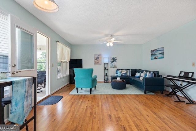 living room featuring baseboards, light wood-style flooring, a textured ceiling, and a ceiling fan