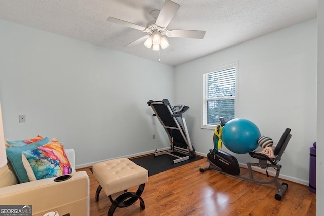 workout room featuring a textured ceiling, wood finished floors, baseboards, and a ceiling fan