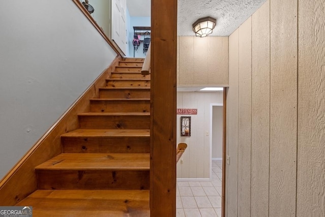 stairway with a textured ceiling, wood walls, and tile patterned flooring