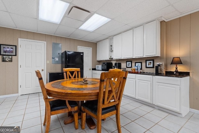 dining area featuring wood walls, baseboards, a drop ceiling, and electric panel