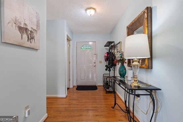 doorway featuring a textured ceiling, wood finished floors, and baseboards