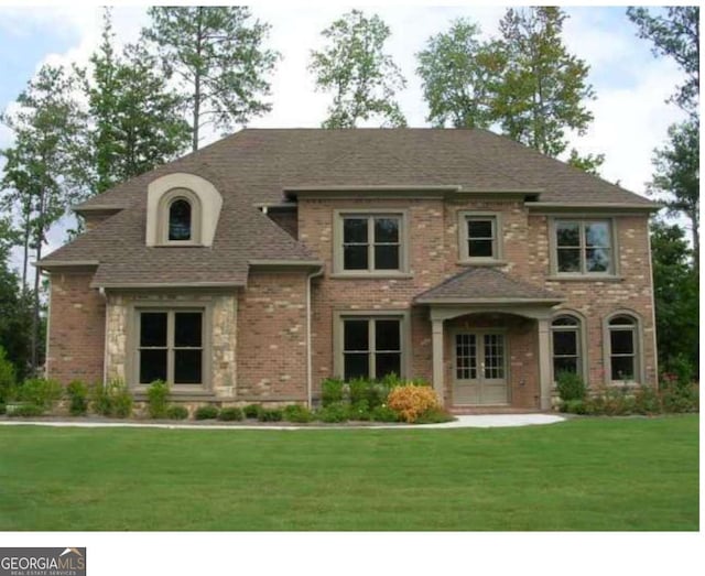 french country style house featuring a front yard, brick siding, french doors, and roof with shingles