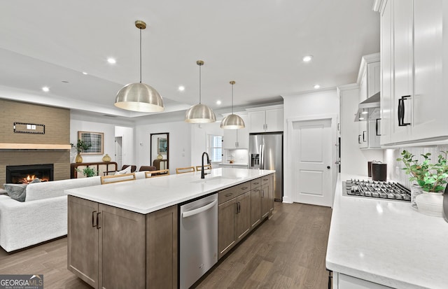 kitchen with a brick fireplace, a sink, open floor plan, appliances with stainless steel finishes, and white cabinetry