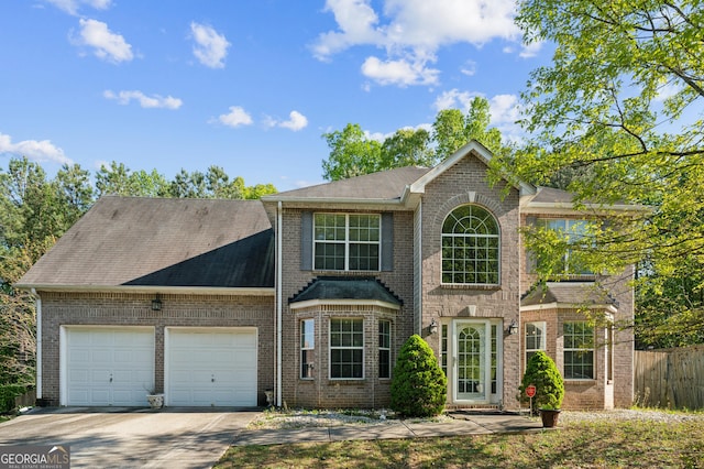 colonial home featuring roof with shingles, driveway, brick siding, a garage, and fence