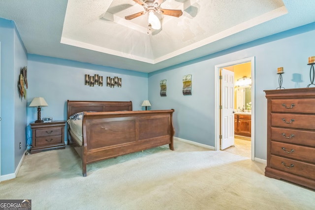 bedroom with a raised ceiling, baseboards, carpet, and ensuite bath
