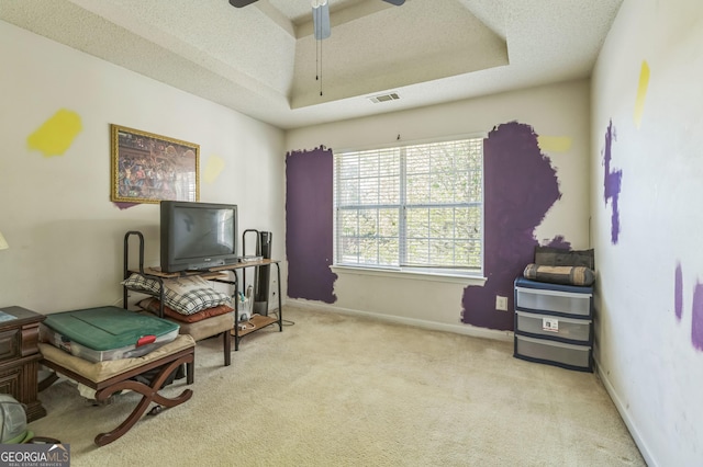 living area with visible vents, ceiling fan, a textured ceiling, a tray ceiling, and carpet floors