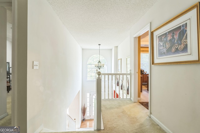 corridor featuring an upstairs landing, a textured ceiling, and carpet