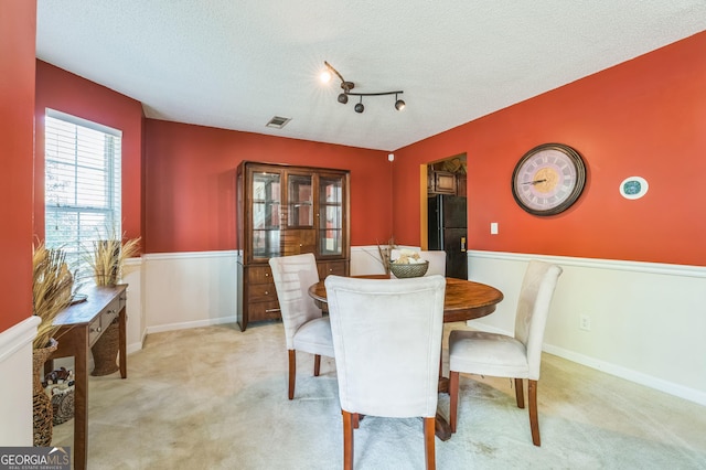 dining space featuring light carpet, visible vents, and a textured ceiling