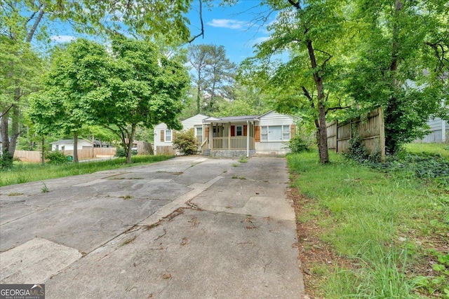 view of front facade featuring concrete driveway, covered porch, and fence