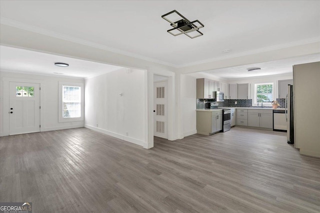 unfurnished living room featuring baseboards, crown molding, light wood-style flooring, and a sink