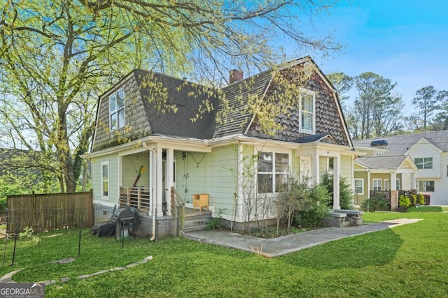 back of house featuring roof with shingles, a gambrel roof, a chimney, and a lawn