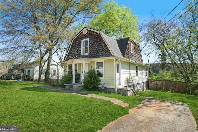 colonial inspired home featuring roof with shingles, a gambrel roof, fence, and a front lawn