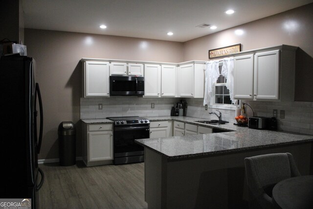 kitchen featuring a sink, a peninsula, light stone counters, range with electric stovetop, and freestanding refrigerator