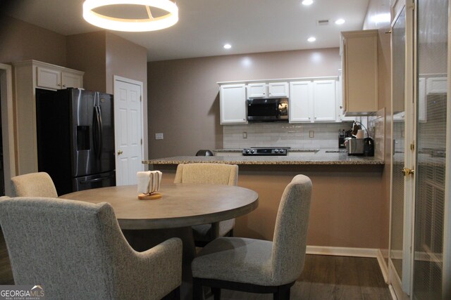 kitchen with stainless steel microwave, fridge with ice dispenser, dark wood-style flooring, tasteful backsplash, and a peninsula