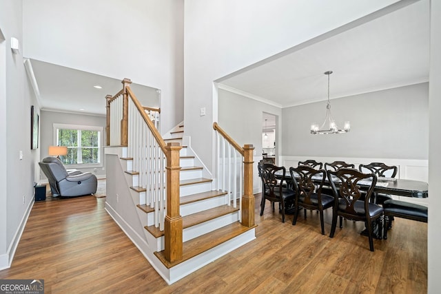 staircase with baseboards, a high ceiling, ornamental molding, a chandelier, and wood finished floors