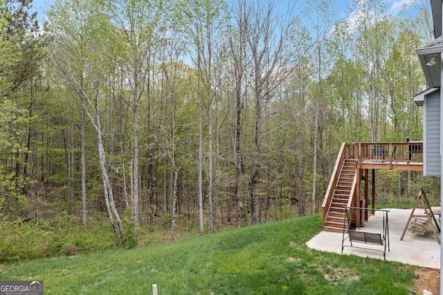 view of yard featuring a wooded view, a patio area, a deck, and stairway