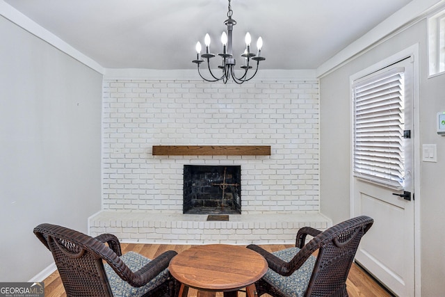 dining room featuring a brick fireplace, a notable chandelier, baseboards, and wood finished floors