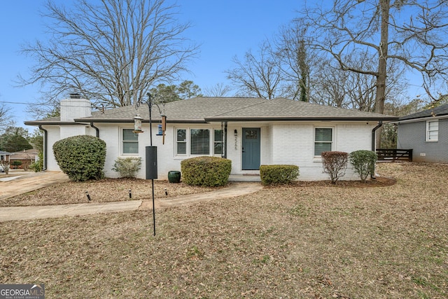 single story home featuring roof with shingles, a chimney, and brick siding
